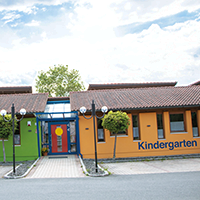 Außenansicht des Kindergartens, oranges Gebäude, rot-blaue Eingangstür, Schriftzug Kindergarten